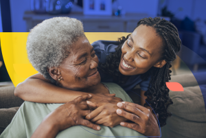 A family caregiver sits beside an elderly parent at home, offering comfort and support. The image conveys care, empathy, and the everyday reality of unpaid family caregiving in the U.S.